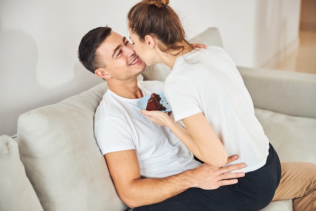 Pareja amorosa abrazándose en el sofá y comiendo pastel de chocolate