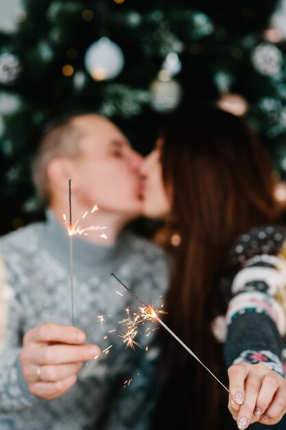 pareja amorosa besándose. Un hombre y una mujer encienden bengalas cerca de un árbol de Navidad. ¡Feliz Navidad y Felices Fiestas! Navidad.