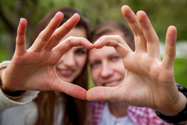 Una pareja amorosa de buen humor en el parque, muestra un corazón de los dedos. Pareja joven, en el parque