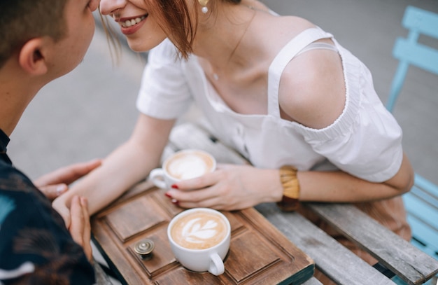 Pareja amorosa con café en la calle en la mesa tomados de la mano sonriendo el uno al otro