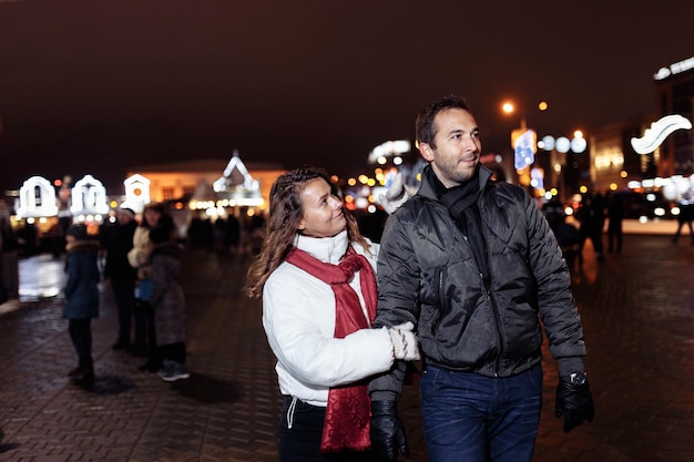 Una pareja amorosa camina por la ciudad navideña nocturna en invierno.