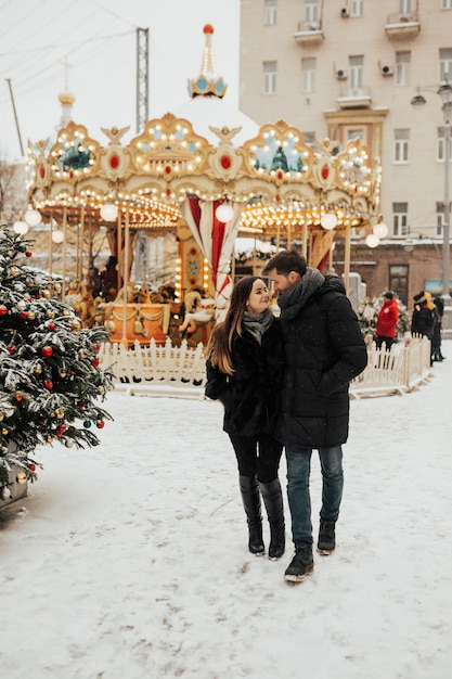 Una pareja amorosa caminando cerca del carrusel en el tiempo de nieve