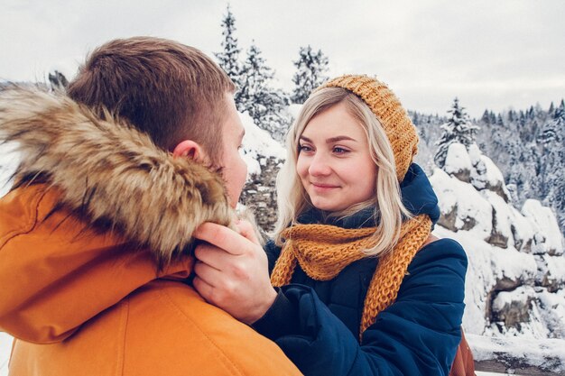 Foto pareja amorosa caricias al aire libre en un paisaje nevado vistiendo abrigos de invierno pesados y gorros de piel.