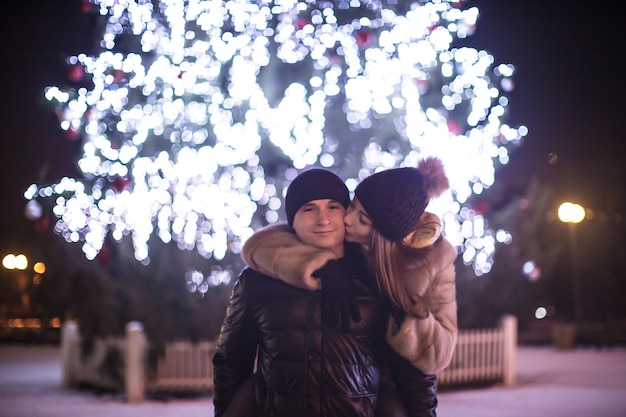 Pareja amorosa cerca del árbol de Navidad en la noche al aire libre