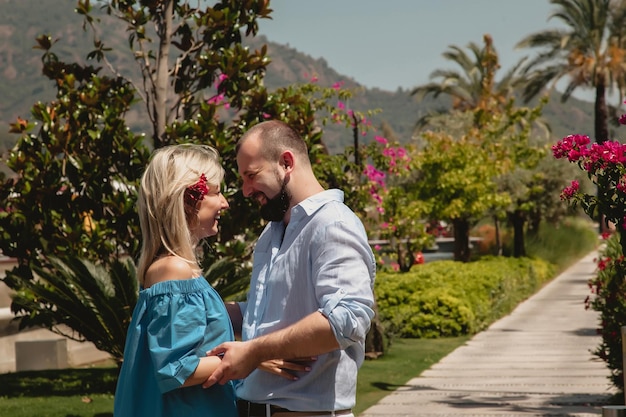 Pareja amorosa disfrutando de la luna de miel en un hotel de lujo caminando por terrenos con palmeras y flores de belleza