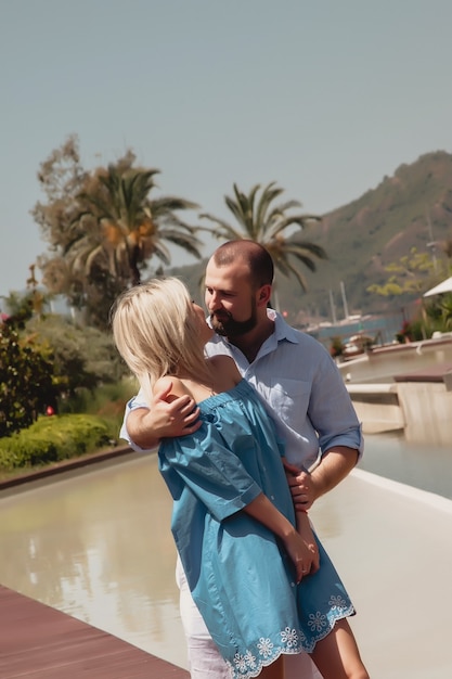 Pareja amorosa disfrutando de su luna de miel en un hotel de lujo, caminando por terrenos con palmeras y piscina