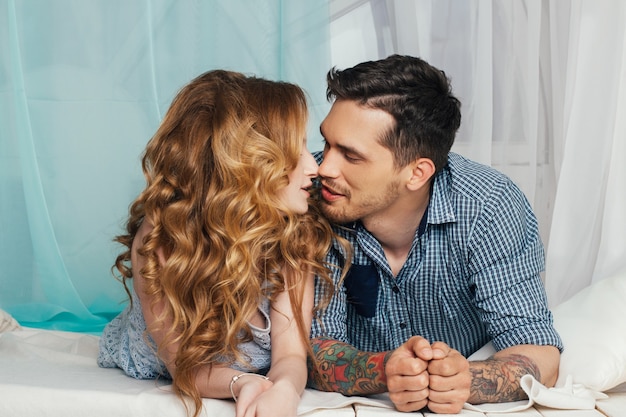 La pareja amorosa se encuentra cerca de la ventana. Sentimientos tiernos y románticos de los recién casados. Bella mujer con cabello largo y un hombre con tatuajes en sus manos