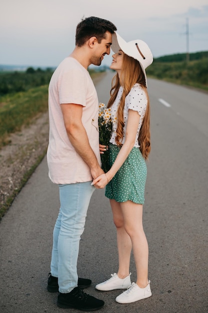 Una pareja amorosa está de pie en medio del camino de viaje tomados de la mano y mirándose...