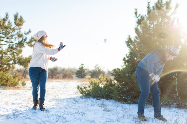 Foto pareja amorosa jugar bolas de nieve en invierno en el bosque. tirarse nieve. ríete y pasa un buen rato