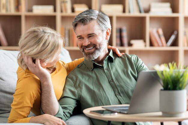 Una pareja amorosa de mediana edad que se une mientras se relaja con una laptop en casa