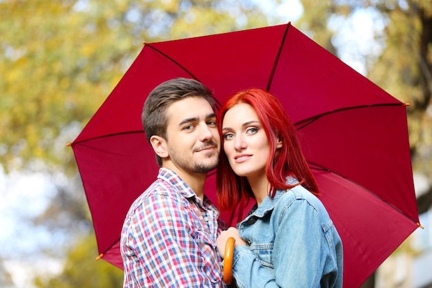 Pareja amorosa bajo un paraguas en el parque de otoño