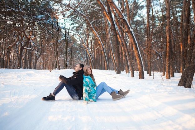 Una pareja amorosa parásito bajo los árboles con el telón de fondo de un bosque nevado de invierno al atardecer