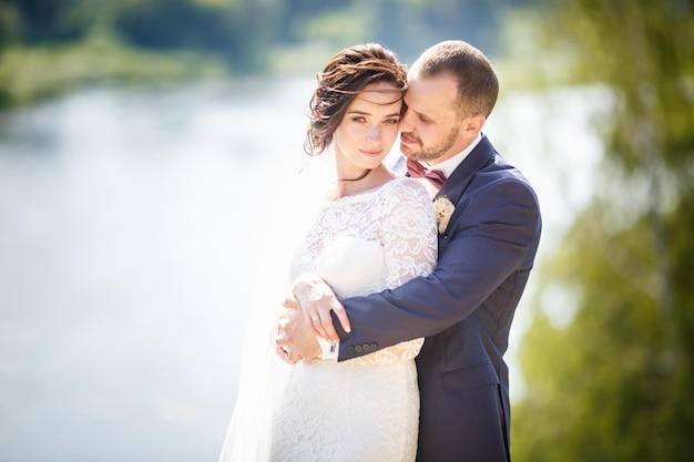 Una pareja amorosa de recién casados camina cerca de un río ancho en un día soleado de verano