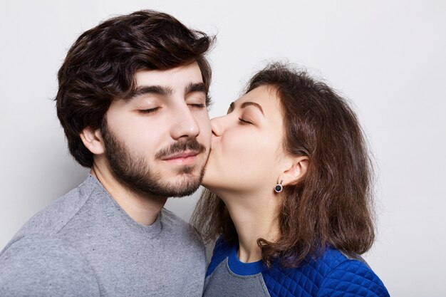 Foto pareja amorosa romántica. una bonita morena besa a su novio barbudo en la barbilla