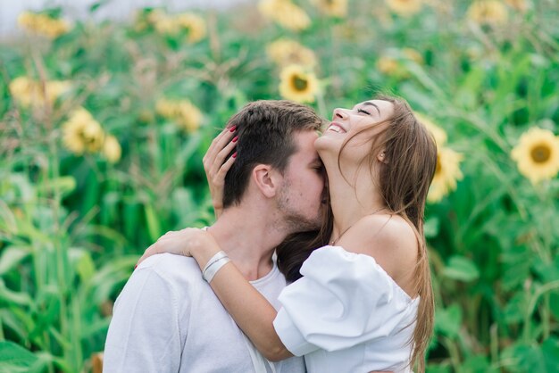 Pareja amorosa en ropa blanca posando en un campo de girasoles