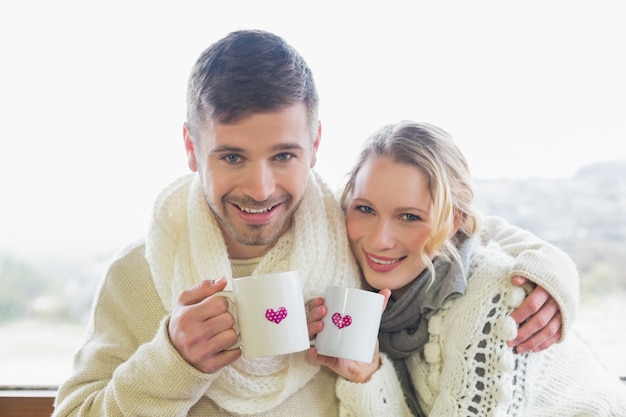 Pareja amorosa en ropa de invierno con tazas de café contra la ventana