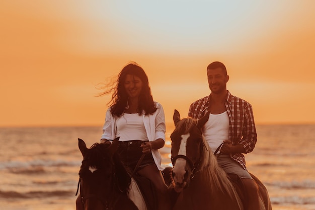 Una pareja amorosa con ropa de verano montando a caballo en una playa de arena al atardecer. Mar y atardecer de fondo. Enfoque selectivo. foto de alta calidad