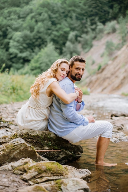 Pareja amorosa sentada en las rocas junto al río en el parque nacional en un día de verano