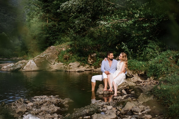 Pareja amorosa sentada en las rocas junto al río en el parque nacional en un día de verano