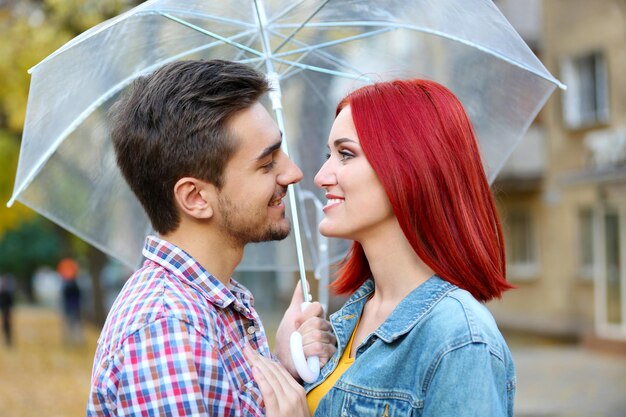 Pareja amorosa bajo una sombrilla en el parque de otoño