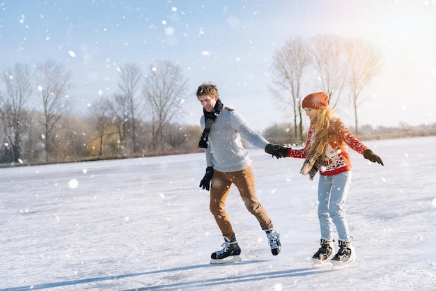 Pareja amorosa en suéteres calientes divirtiéndose en el hielo mujer y hombre patinaje sobre hielo al aire libre en el soleado nevado