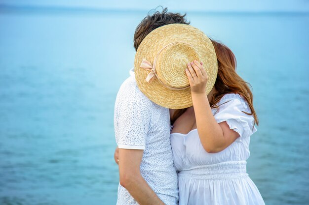 Foto la pareja amorosa tiene un beso escondido detrás del sombrero de paja amarillo en el fondo del mar. amor irreconocible de mujer y hombre, relación romántica del día de san valentín en luna de miel. banner web largo con espacio de copia.