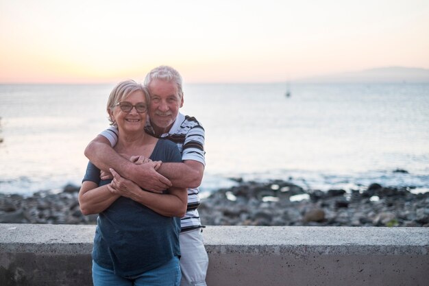 Pareja de ancianos acaparando en la playa con mucho amor - jubilados juntos - mujer con gafas y hombre con fondo de mar