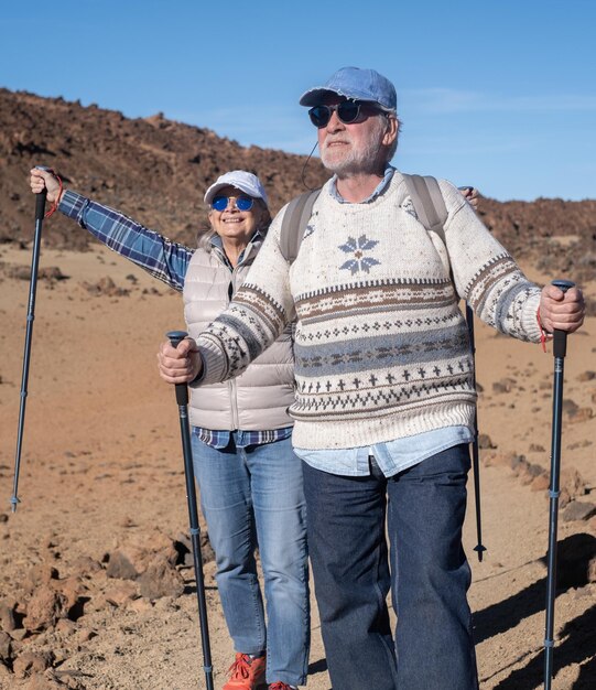 Una pareja de ancianos activos y despreocupados con mochila caminando al aire libre con la ayuda de postes disfrutando de la naturaleza