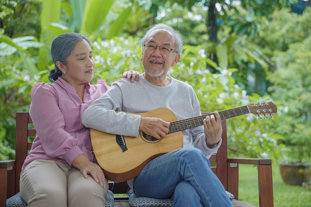 Pareja de ancianos asiáticos anciano tocando la guitarra mientras su esposa canta juntos al aire libre en casa Actividad atención médica familiar Disfrutando del estilo de vida durante la vida de jubilación divirtiéndose de los mayores