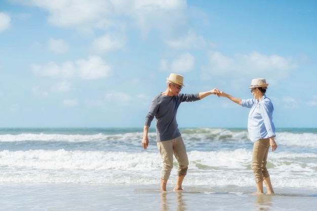 Foto pareja de ancianos asiáticos bailando en la playa. luna de miel de ancianos juntos muy feliz después de la jubilación. plan de seguro de vida. actividad después de la jubilación en verano