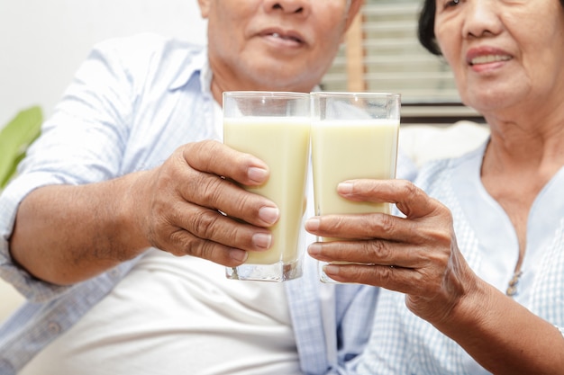 Pareja de ancianos asiáticos bebe leche rica en calcio para prevenir la osteoporosis.