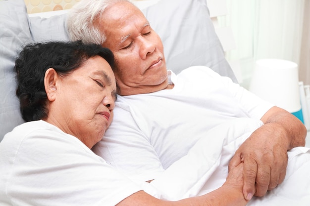 Una pareja de ancianos asiáticos duerme acurrucada en la cama en el concepto familiar de dormitorio seguro de salud para personas mayores