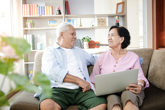 Pareja de ancianos asiáticos sentados en el sofá y usando laptop