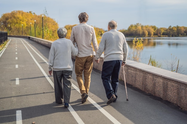 Una pareja de ancianos camina por el parque con un asistente masculino o un nieto adulto. Cuidado de personas mayores, voluntariado.