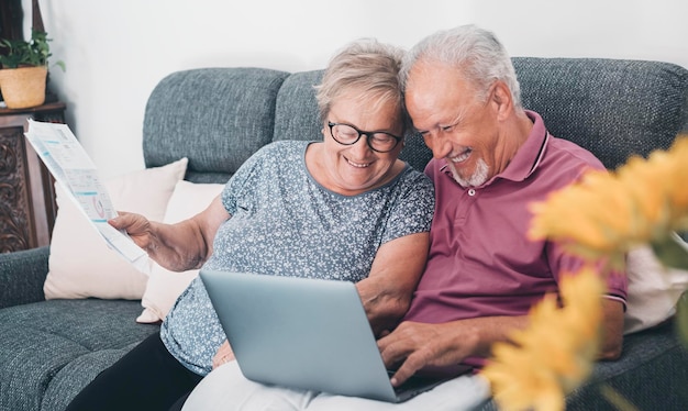 Pareja de ancianos en casa pagando facturas en línea con una computadora portátil y riéndose mucho divirtiéndose juntos Felicidad y estilo de vida de los ancianos Hombre y mujer mayores sentados en un sofá con conexión de computadora en línea