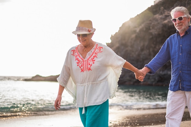 Pareja de ancianos caucásicos hermoso hombre y mujer cabello blanco y sombrero caminar juntos en la playa disfrutando de la nueva vida adulta jubilada tercera edad con libertad del trabajo y oficinas