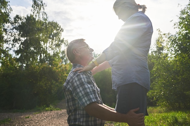 Una pareja de ancianos enamorados en una cita romántica en un parque de verano sonriendo y abrazándose contra un fondo de árboles verdes