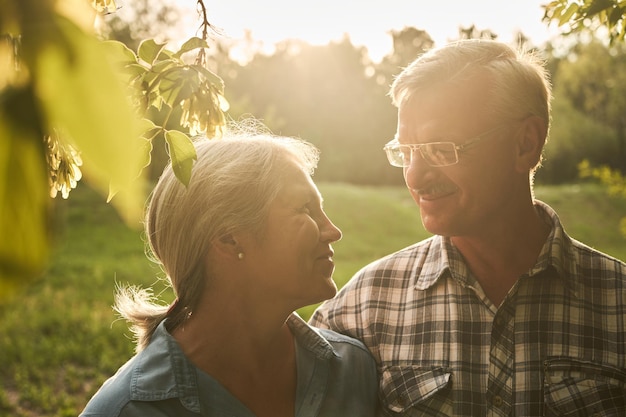 Una pareja de ancianos enamorados en una cita romántica en un parque de verano sonriendo y abrazándose contra un fondo de árboles verdes