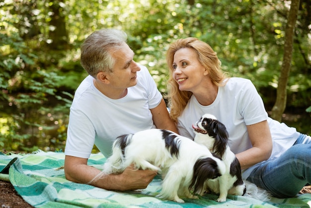 Una pareja de ancianos se está relajando en un picnic en el bosque y jugando con un perro en una manta