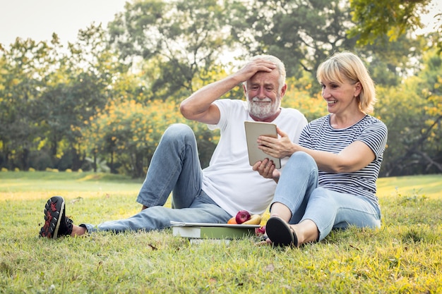 Pareja de ancianos está sentado en una tableta en el parque.