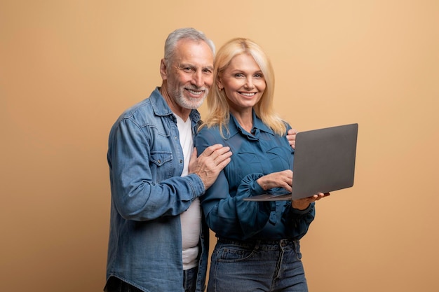 Una pareja de ancianos jubilados positivos usando una computadora portátil sobre un fondo beige
