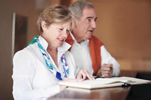 Una pareja de ancianos leyendo y firmando documentos en la recepción del hotel para reservar reservas o vacaciones Un hombre y una mujer maduros llenando formularios de solicitud o comprobando papeles o registrándose en el complejo