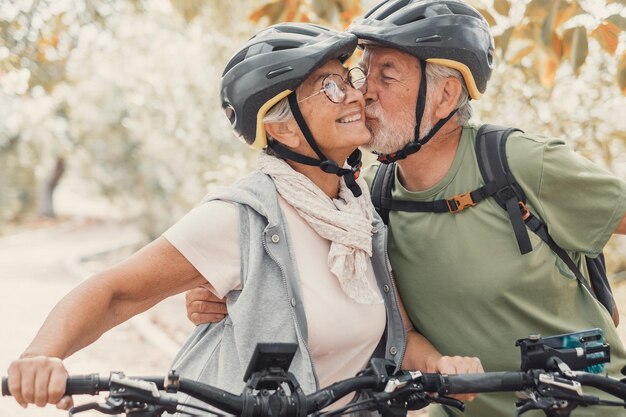 Una pareja de ancianos lindos y dulces enamorados disfrutando juntos de la naturaleza al aire libre divirtiéndose con bicicletas un anciano besando a su esposa sonriendo y sintiéndose bien