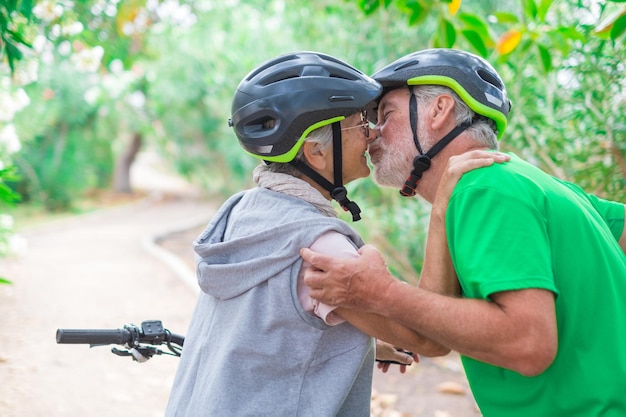 Una pareja de ancianos lindos y dulces enamorados disfrutando juntos de la naturaleza al aire libre divirtiéndose con bicicletas un anciano besando a su esposa sonriendo y sintiéndose bien