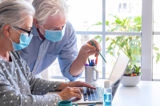 Foto pareja de ancianos con máscara contra la gripe usando una computadora portátil en casa