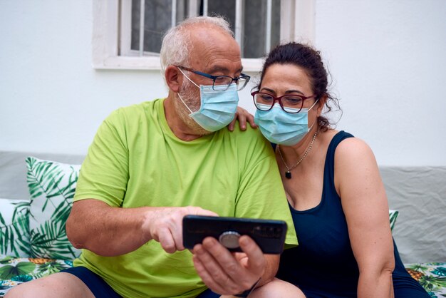 Una pareja de ancianos con máscaras faciales y haciendo una videollamada con una tableta