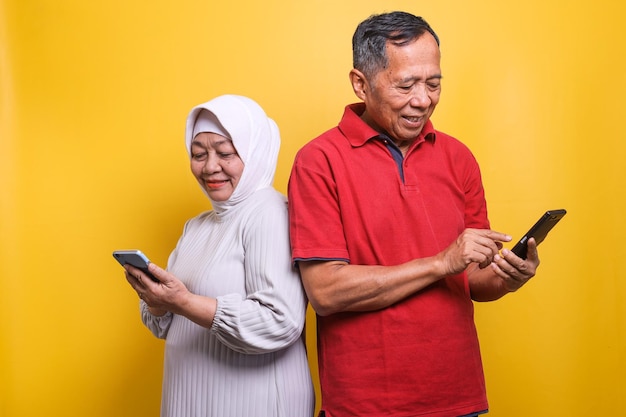 Una pareja de ancianos modernos mirando un teléfono inteligente mientras están de pie contra un fondo amarillo