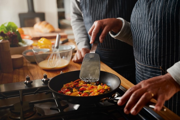 Una pareja de ancianos multiculturales frita verduras con una espátula en una sartén en una estufa moderna