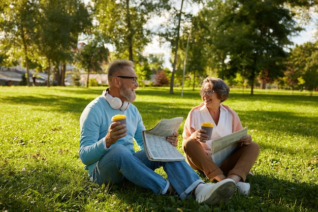 Una pareja de ancianos relajándose al aire libre leyendo el periódico en el parque