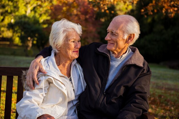 Pareja de ancianos sentados en un banco sonriendo el uno al otro en el parque